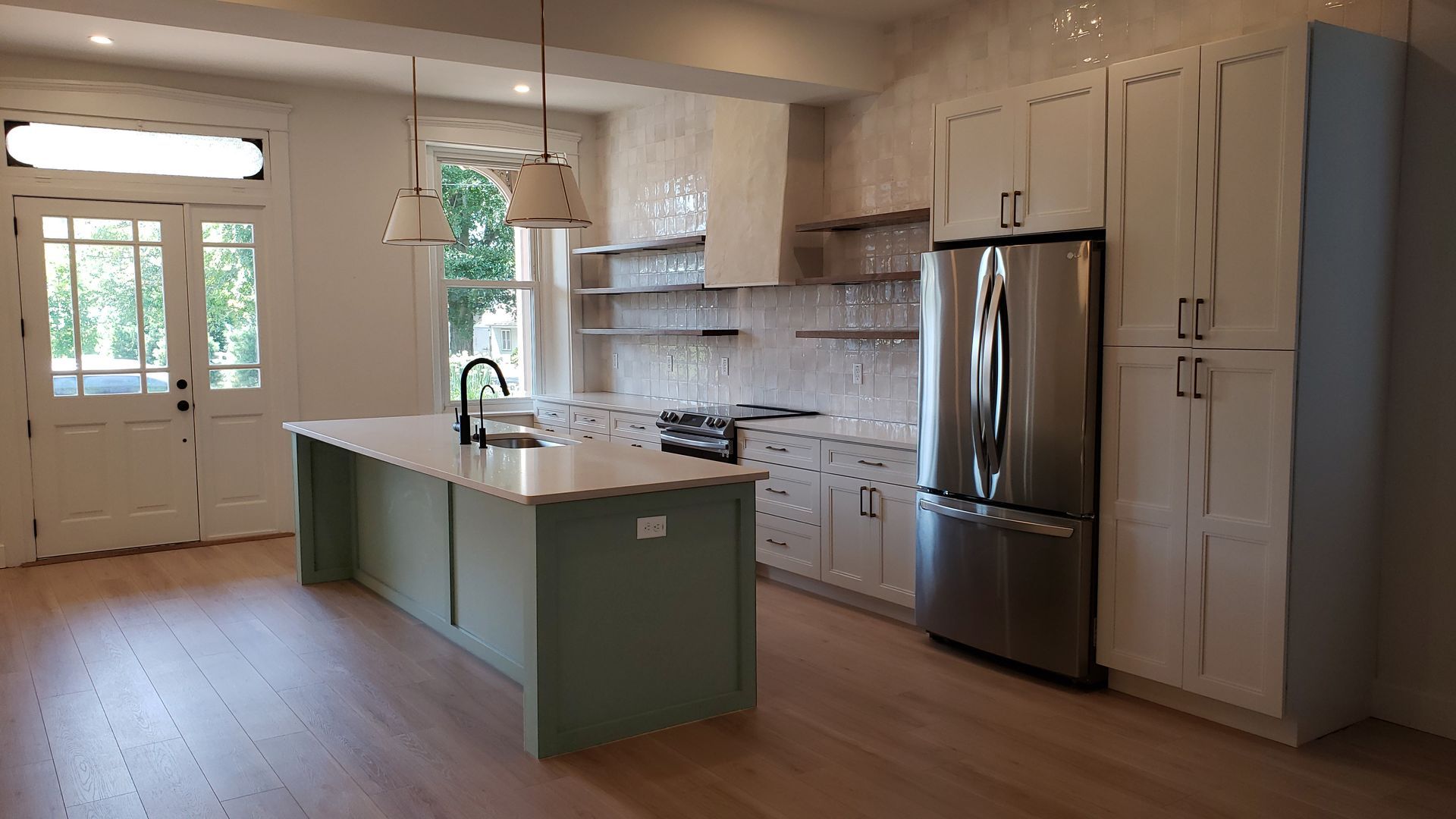 Bright kitchen with white cabinets, stainless steel fridge, green island, and glass doors to the outside.