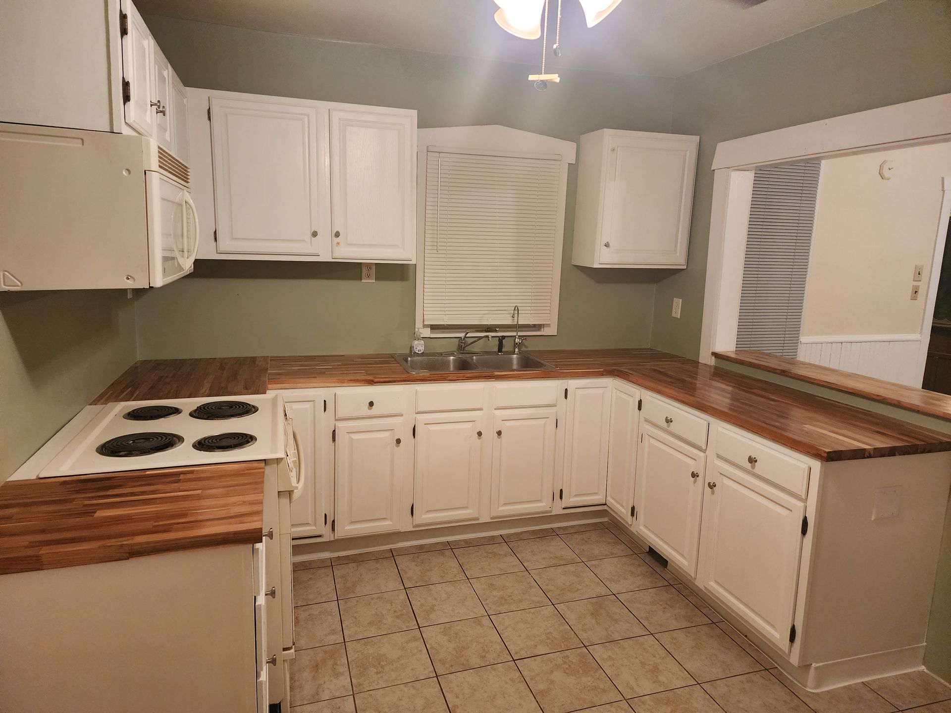 Small kitchen with white cabinets, wood countertops, tiled floor, and a stove under a window