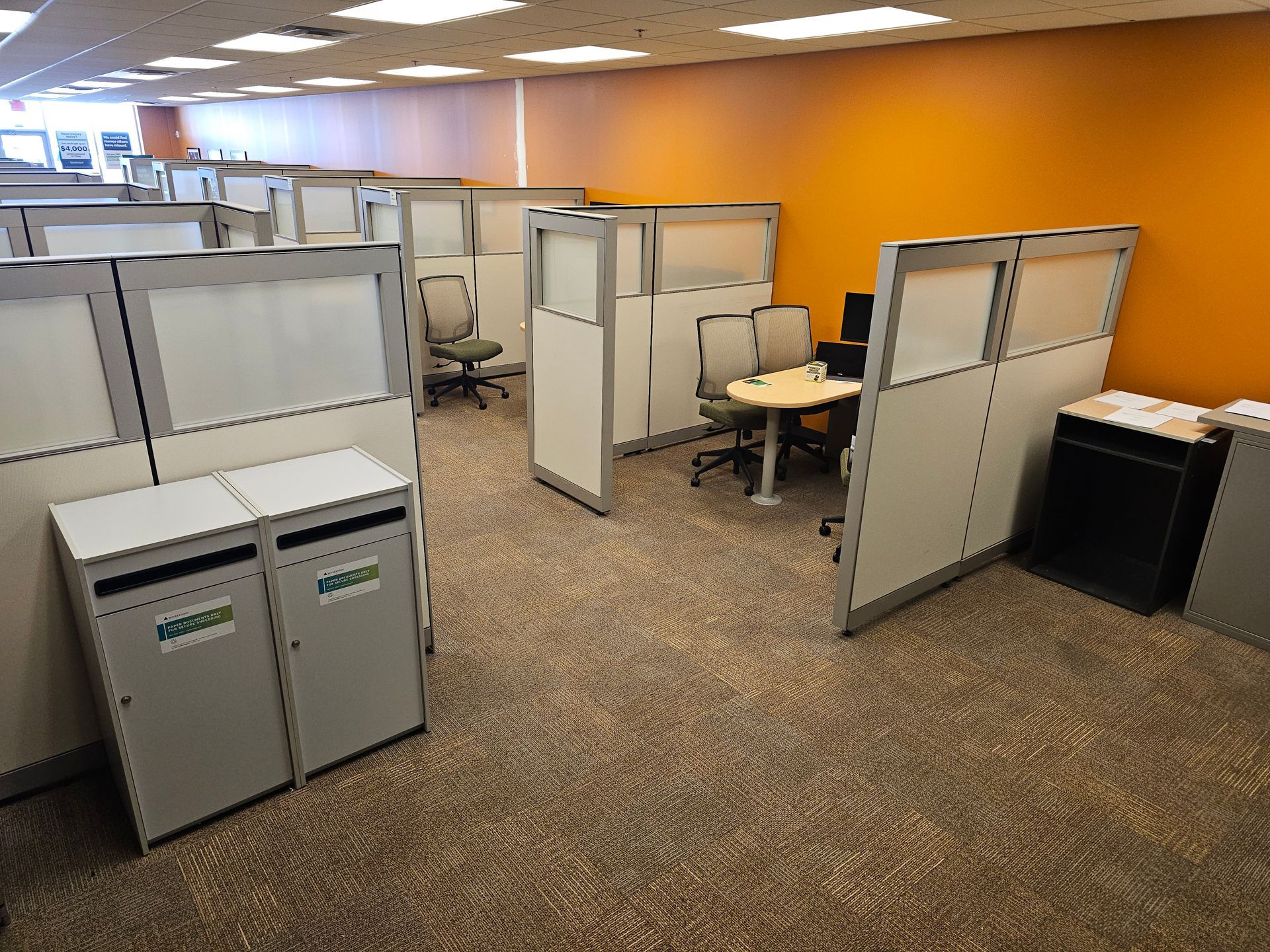 Office cubicles in an empty workspace with beige partitions, carpet, and orange wall accents