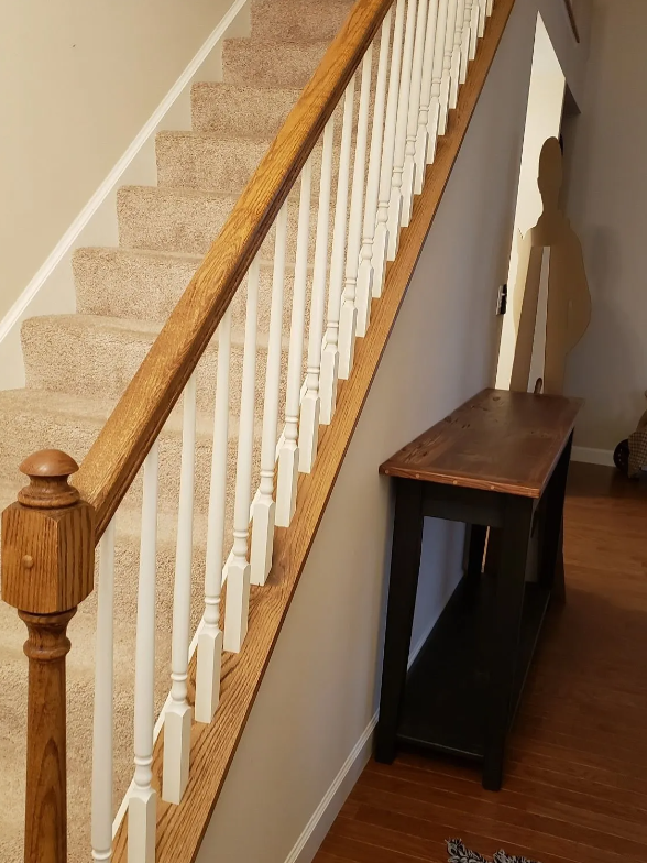 Staircase with beige carpet, white balusters, wooden handrail, and a small dark table at the bottom.
