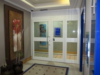 A bright office foyer with white glass doors, potted plants, and abstract artwork hanging on the walls.