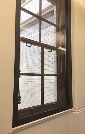 A rectangular window with a dark wooden frame and a central muntin, looking out onto a white brick wall.