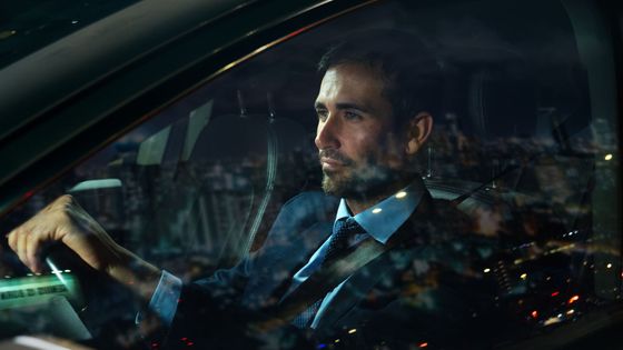 A man in a suit and tie is driving a car at night.