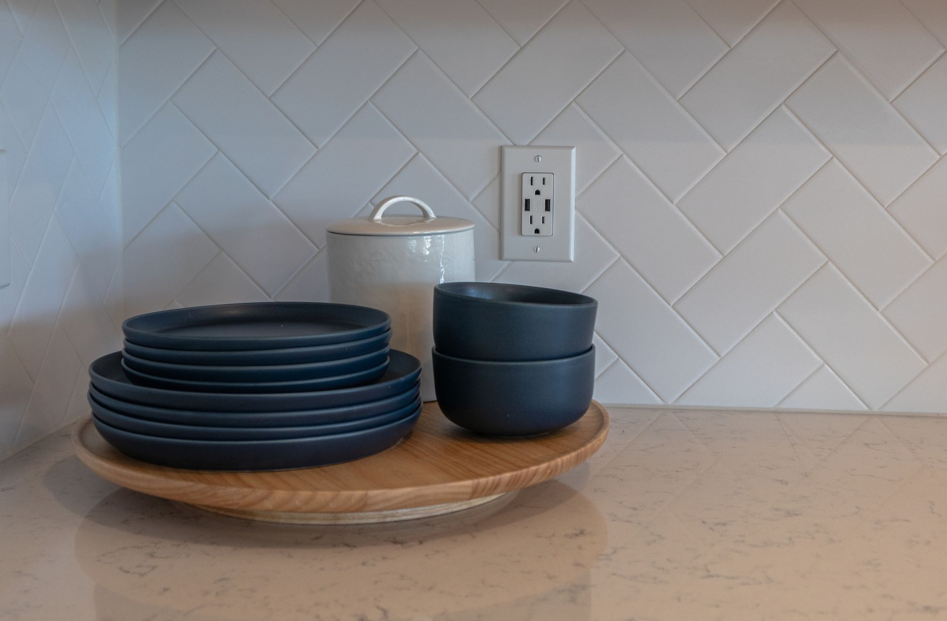 A stack of plates and bowls on a wooden tray on a kitchen counter.