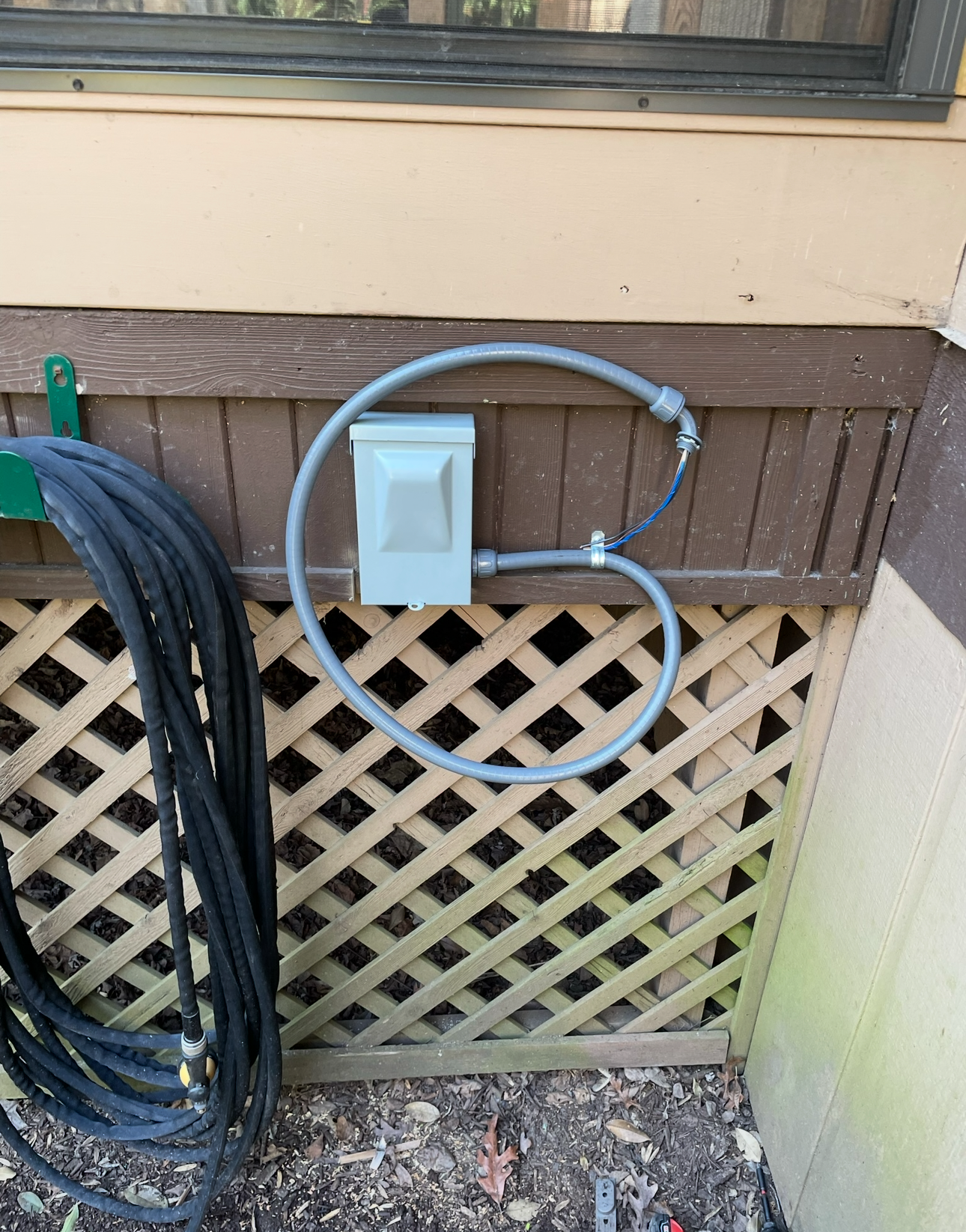 A hose is hanging on a wall next to a power outlet.