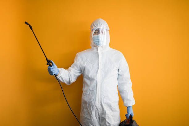 A person in protective gear holding a sprayer against a bright orange background.