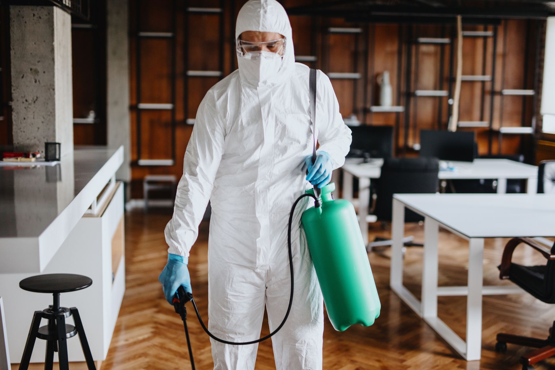 An exterminator in a protective suit and face mask spraying in an empty office.