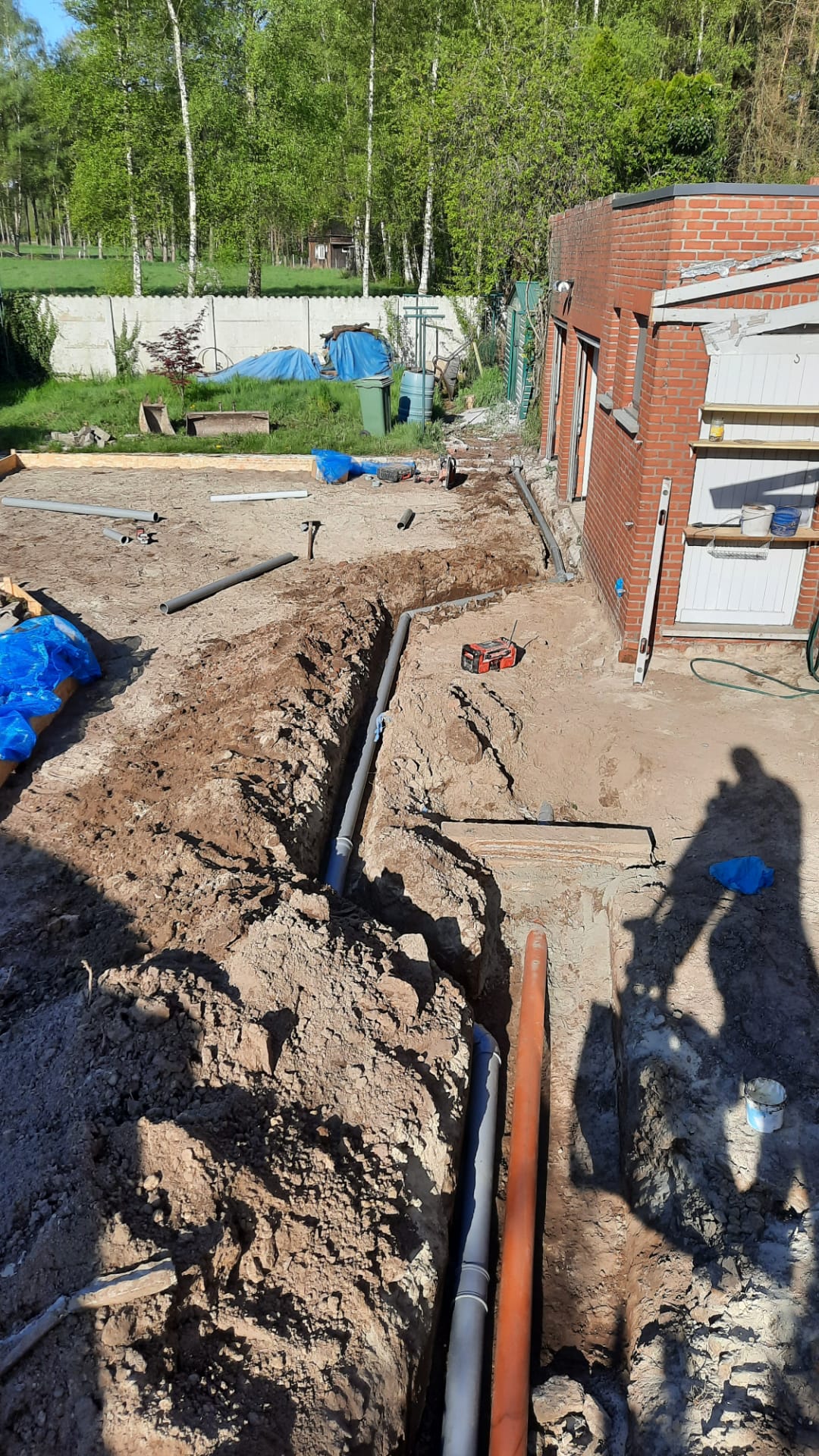 Een man graaft een gat in de grond voor een bakstenen gebouw.