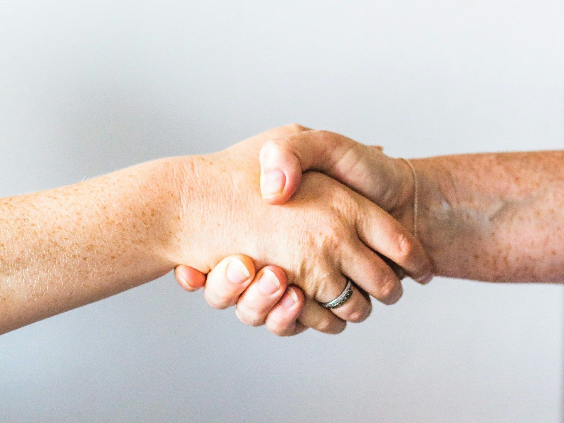 Een close-up van twee mensen die elkaar de hand schudden met ringen aan hun vingers.