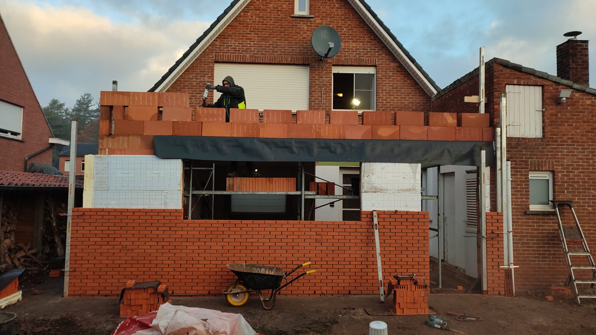 Aan de zijkant van een huis wordt een bakstenen muur gebouwd.