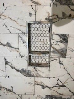 Shower niche with marble-look tile surround and honeycomb tile backing.