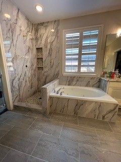 Bathroom with marble-like tile, shower, built-in tub, and window with blinds.