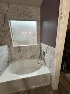 Bathroom with white tub, marble-patterned tile, frosted window, and purple wall.