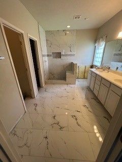 Spacious bathroom with marble-look tile flooring and shower. Double vanity with a large mirror and natural light.