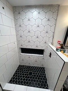 Modern bathroom shower with black and white patterned tiles. Black hexagon floor tiles and decorative wall.