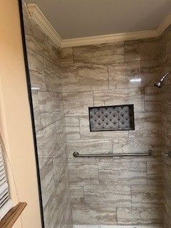 Shower with light brown tiled walls, a handrail, and a built-in shelf.