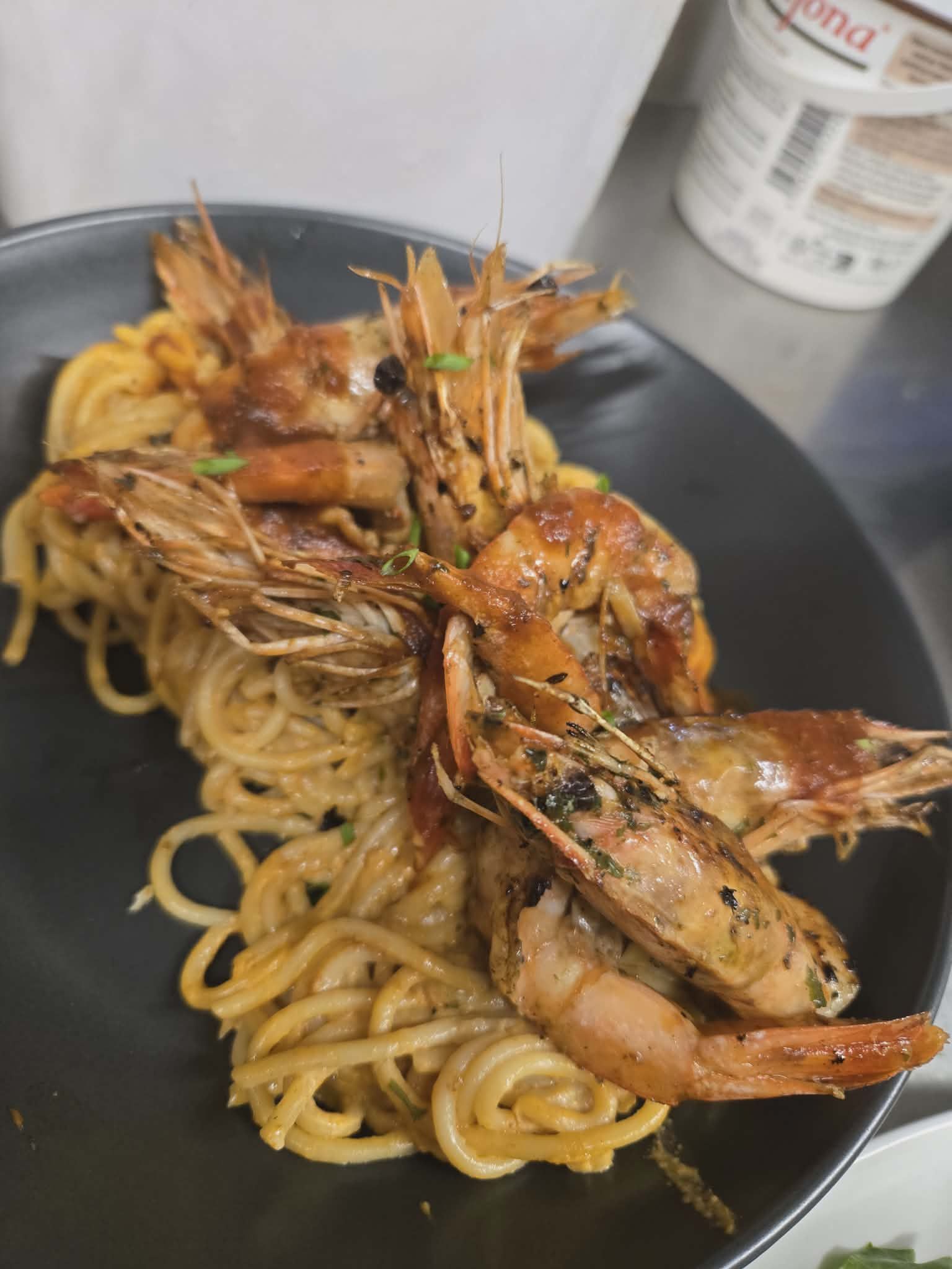 A portion of spaghetti served with several large, seasoned, whole sautéed shrimp on a dark plate.