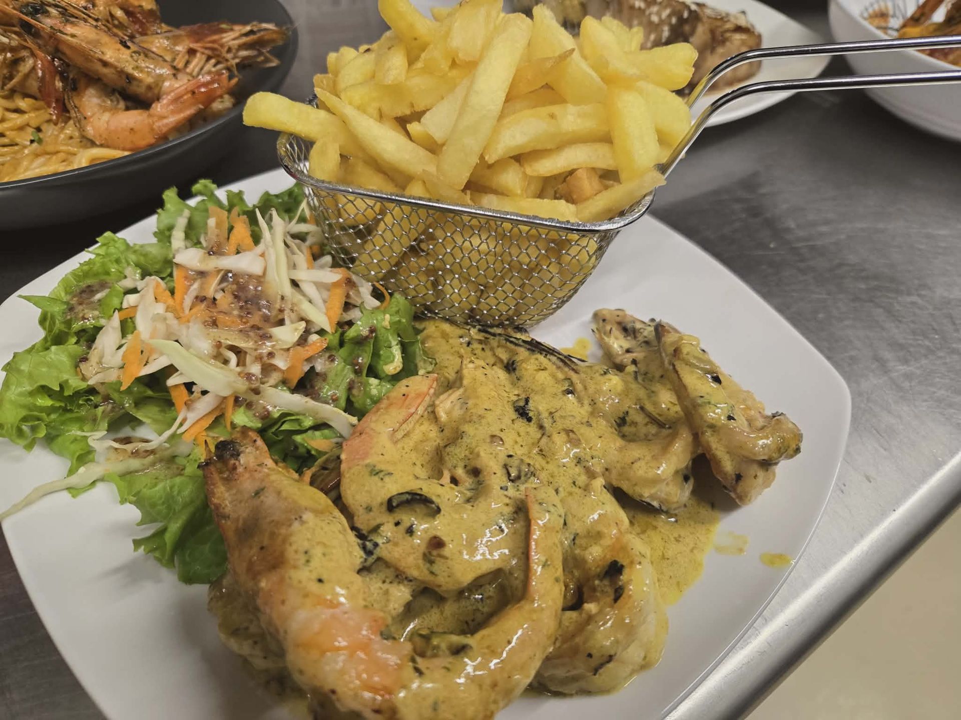 A plate with shrimp in a creamy sauce, a side salad, and a wire basket of french fries on a kitchen counter.