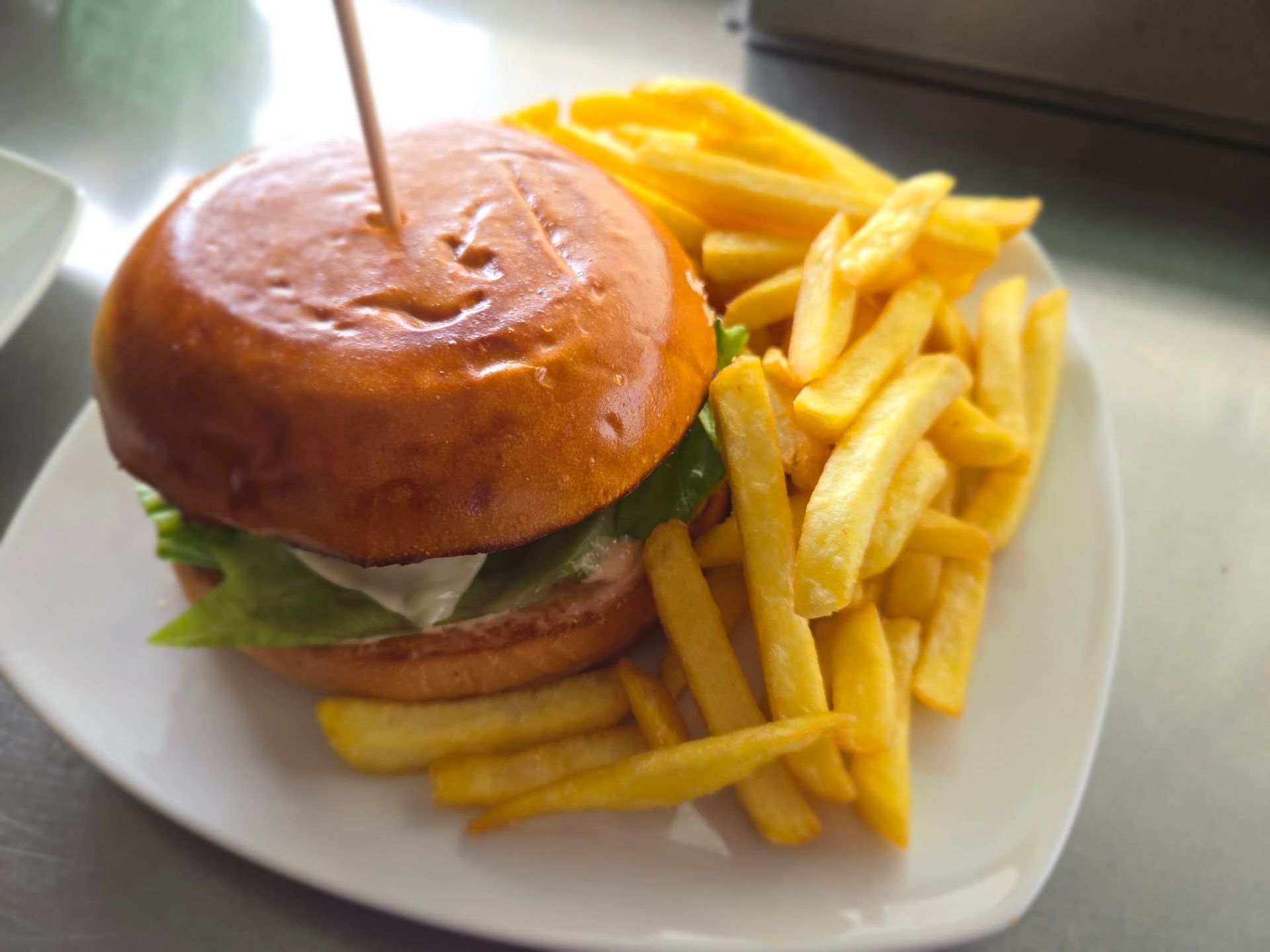 A burger with lettuce held by a toothpick, served with a pile of golden french fries on a white plate.