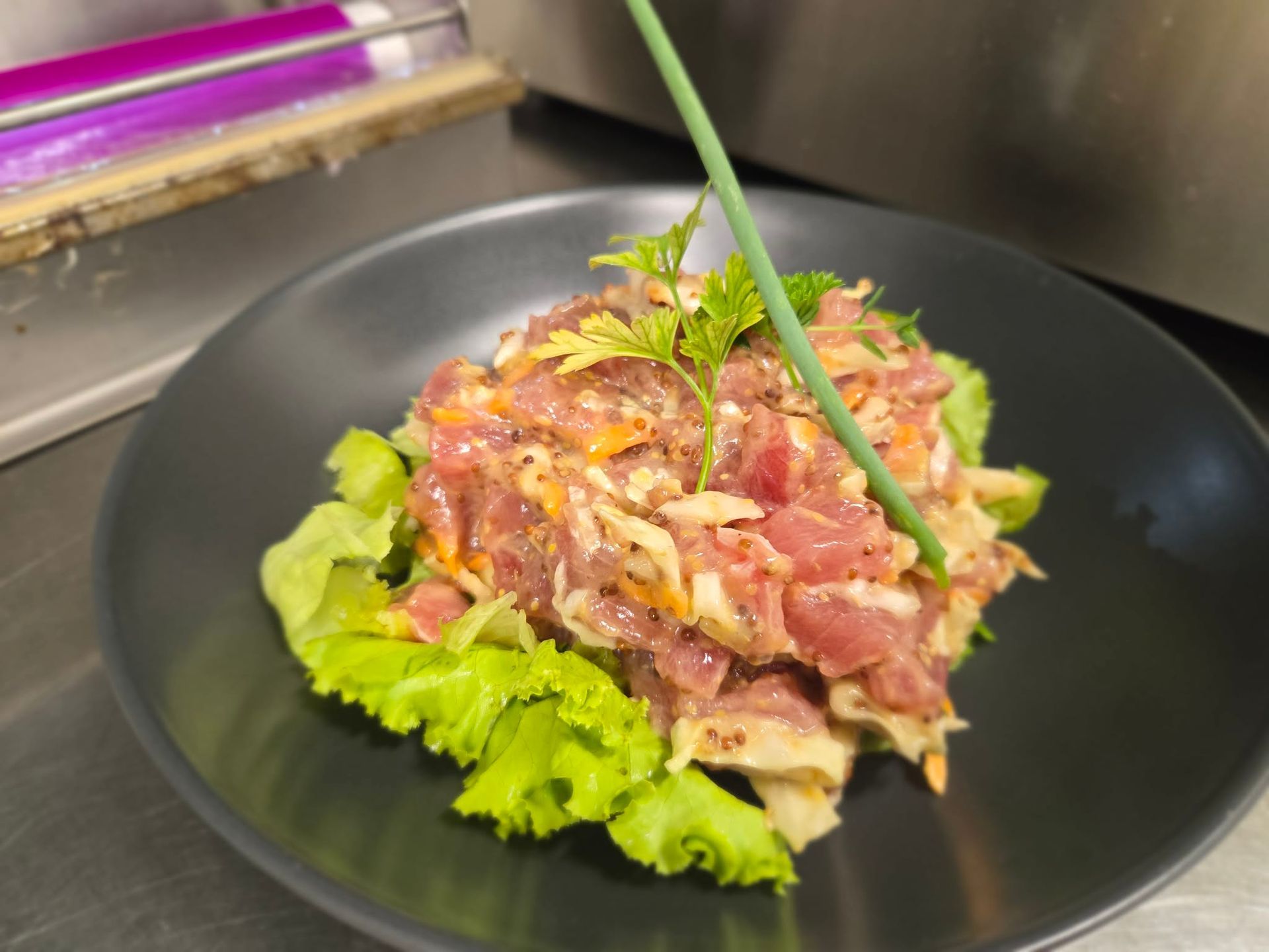 A plate of tuna tartare garnished with fresh herbs and chives, resting on a bed of lettuce in a black bowl.