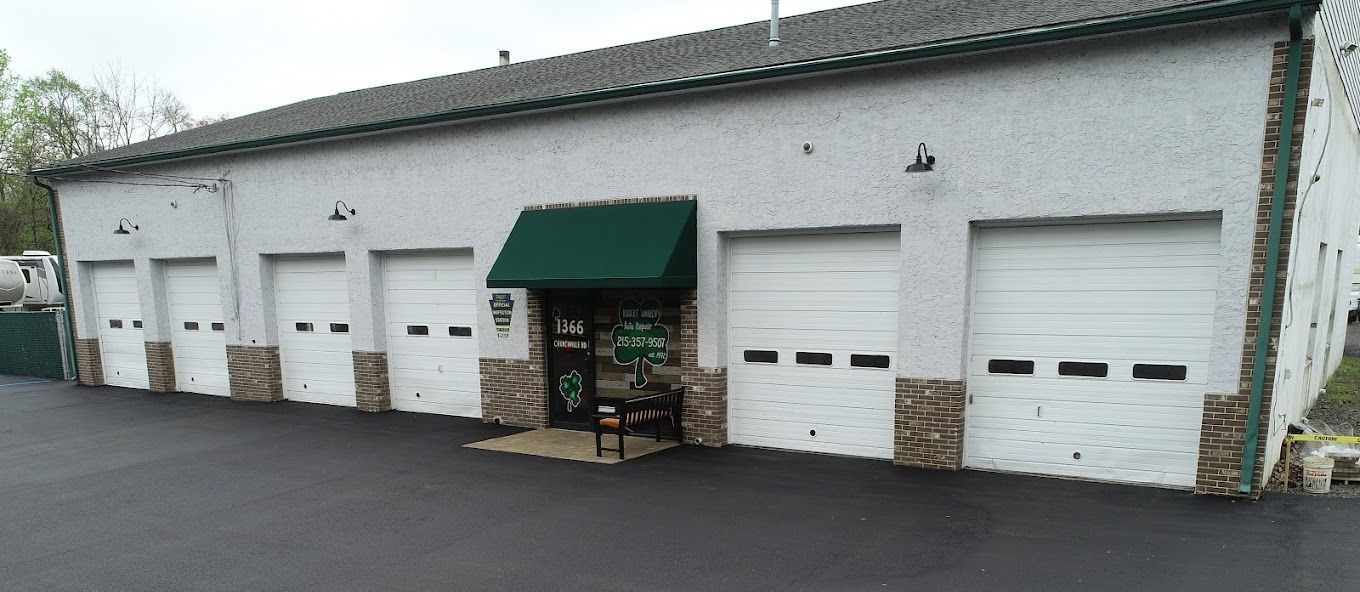 A white commercial building with garage doors and a green awning. The building sits on a black asphalt surface.