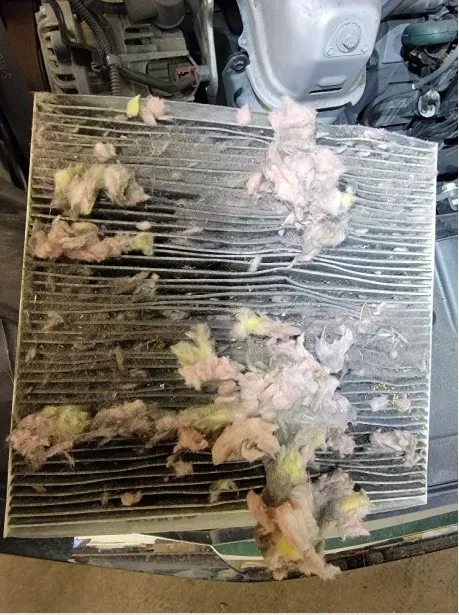 Dirty air filter covered in pink and yellow debris; in a car engine bay.