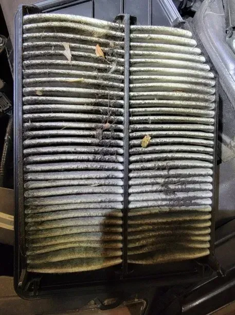 Dirty air filter in a car, showing layers of accumulated dirt and debris.