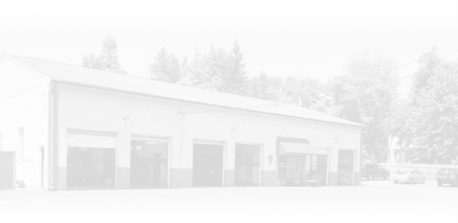 White building with garage doors, trees, and vehicles outside.