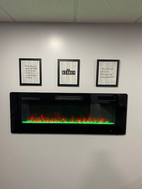 Electric fireplace with green and orange lights, three framed quotes above it on a white wall.