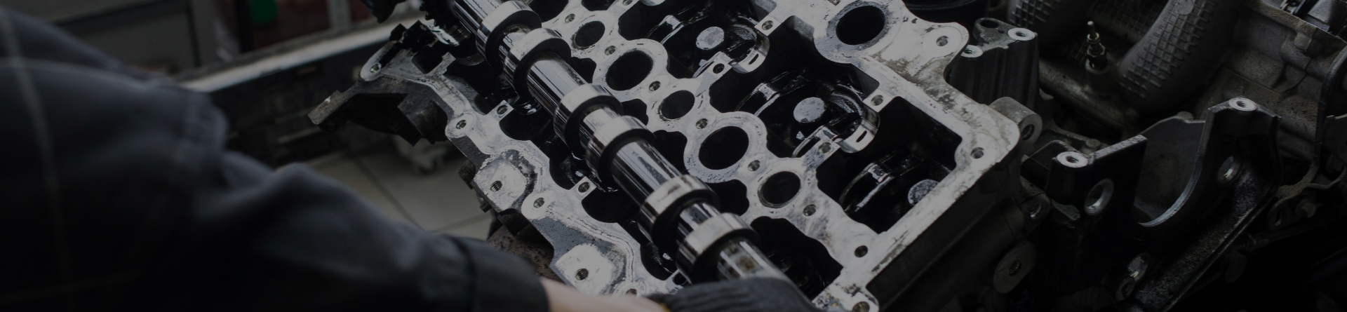 A person is working on a car engine cylinder head in an automotive setting.