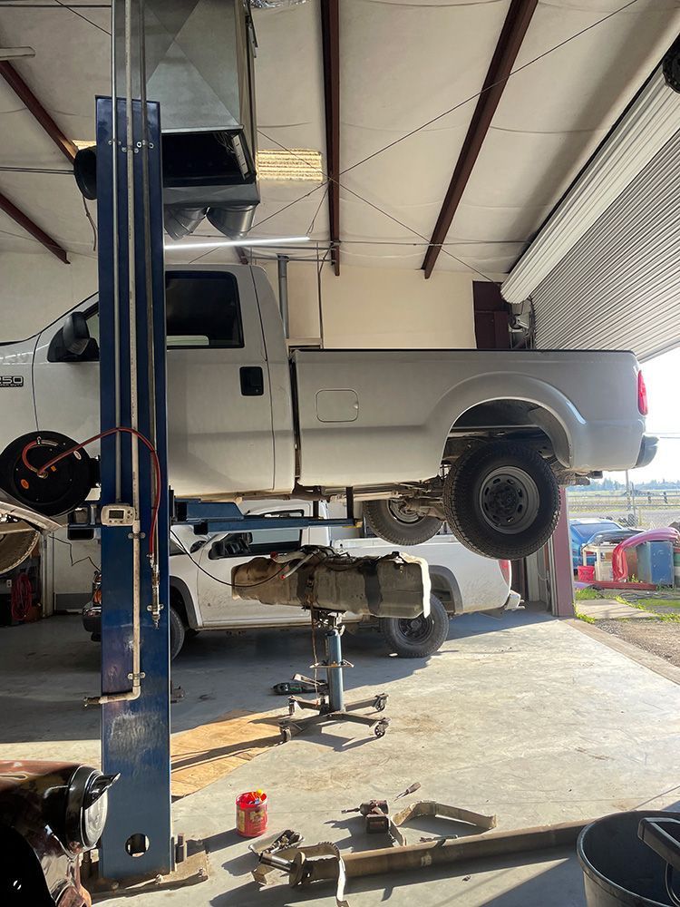 White truck raised on a lift in a garage, a mechanic likely working on it.