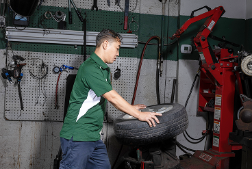 Mechanic in green shirt handles tire in a garage, near tire changing equipment.