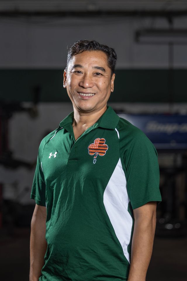 Man in green polo shirt smiles, posing inside what appears to be a workshop.