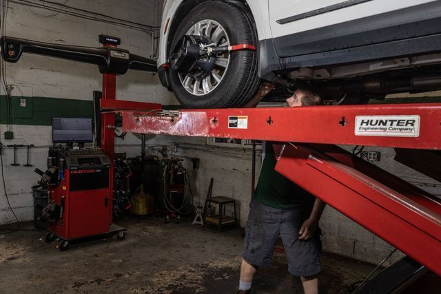 A car being aligned in a repair shop; a mechanic works under it while it's on a lift. Red Hunter equipment.