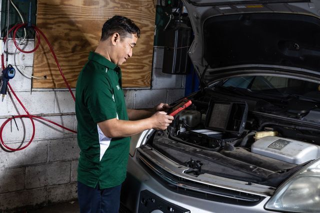 Mechanic checks car engine with a red device in a garage.