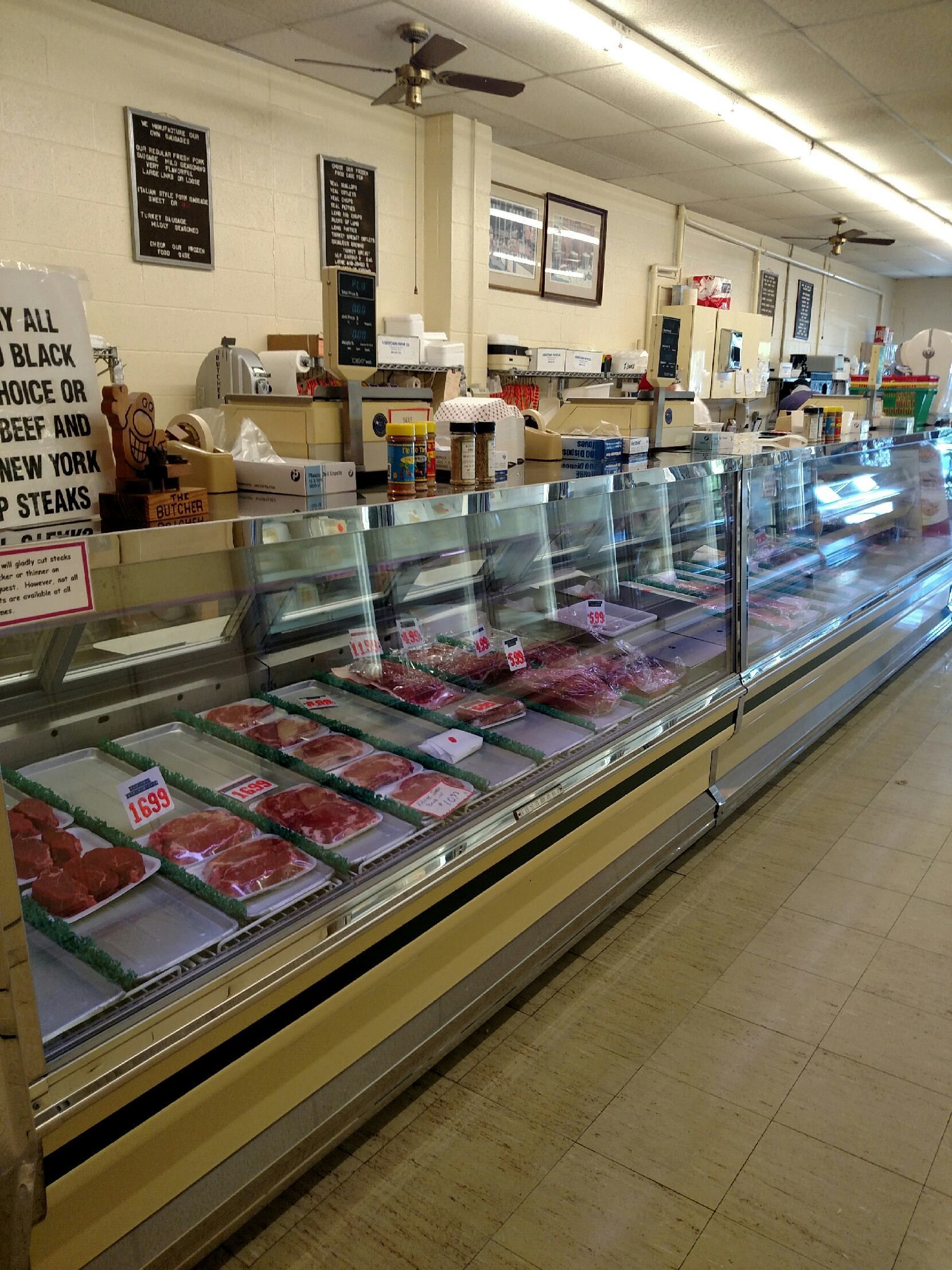 Long meat display case in a small butcher shop, with red cuts of meat and a counter behind it