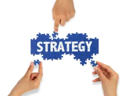A group of people are putting together a puzzle with the word strategy written on it.
