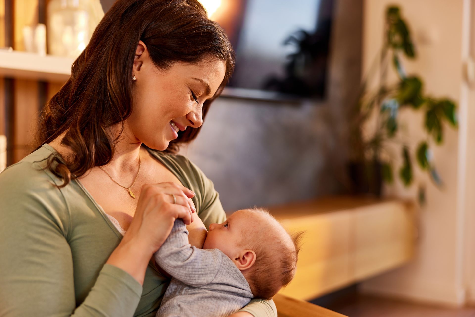 A woman is breastfeeding her baby in a living room.