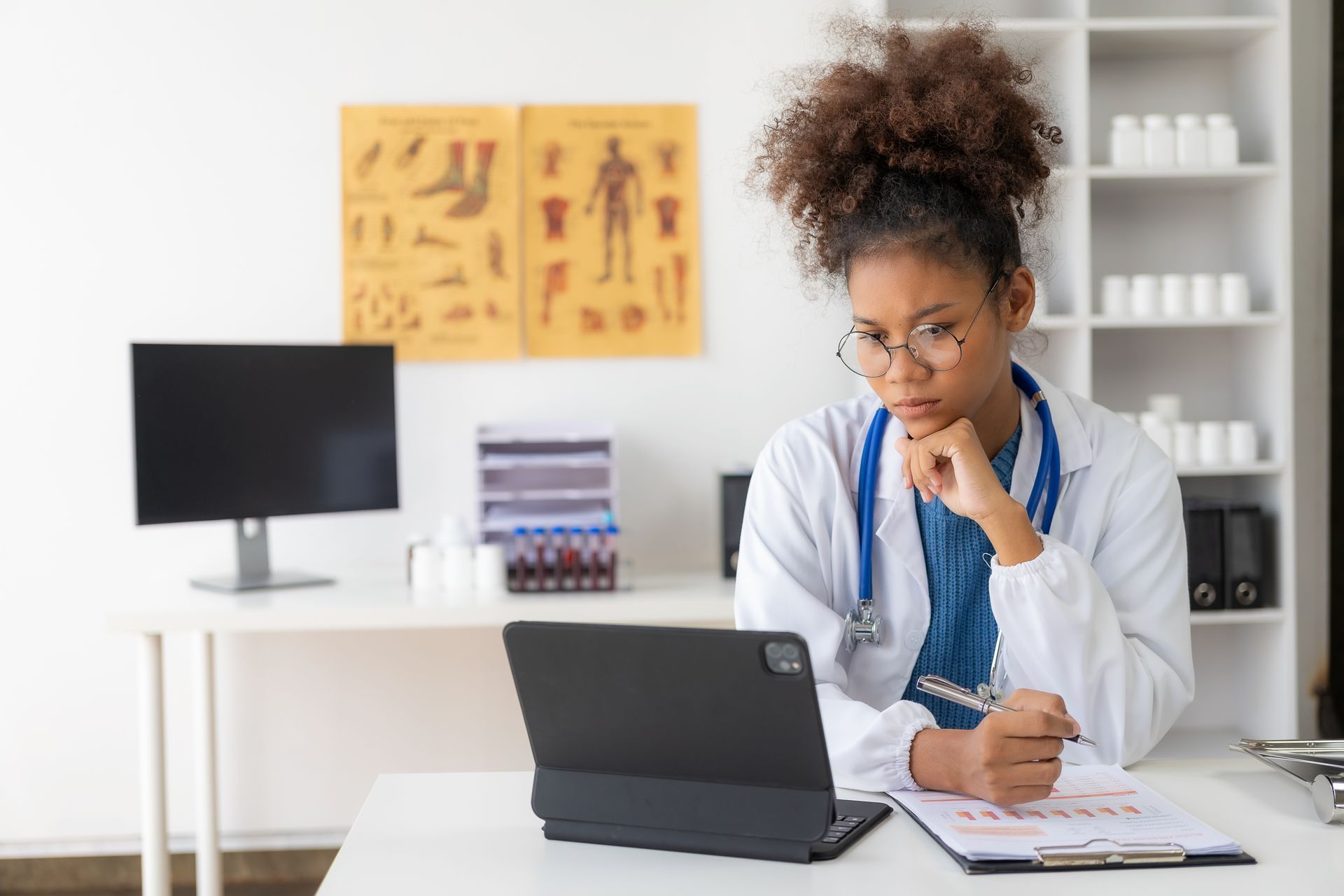 A female doctor is sitting at a desk using a laptop computer.