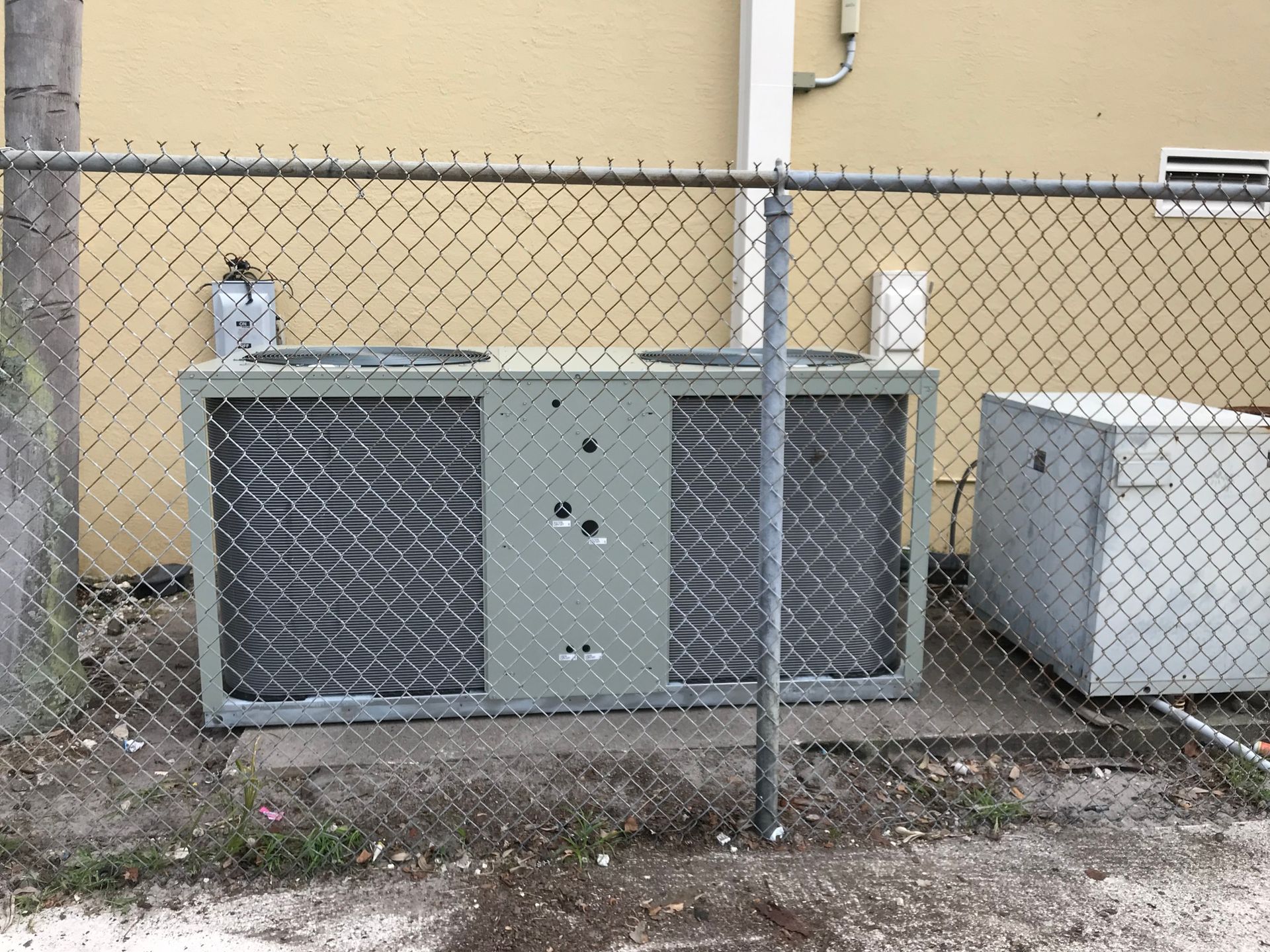 An air conditioner is behind a chain link fence.