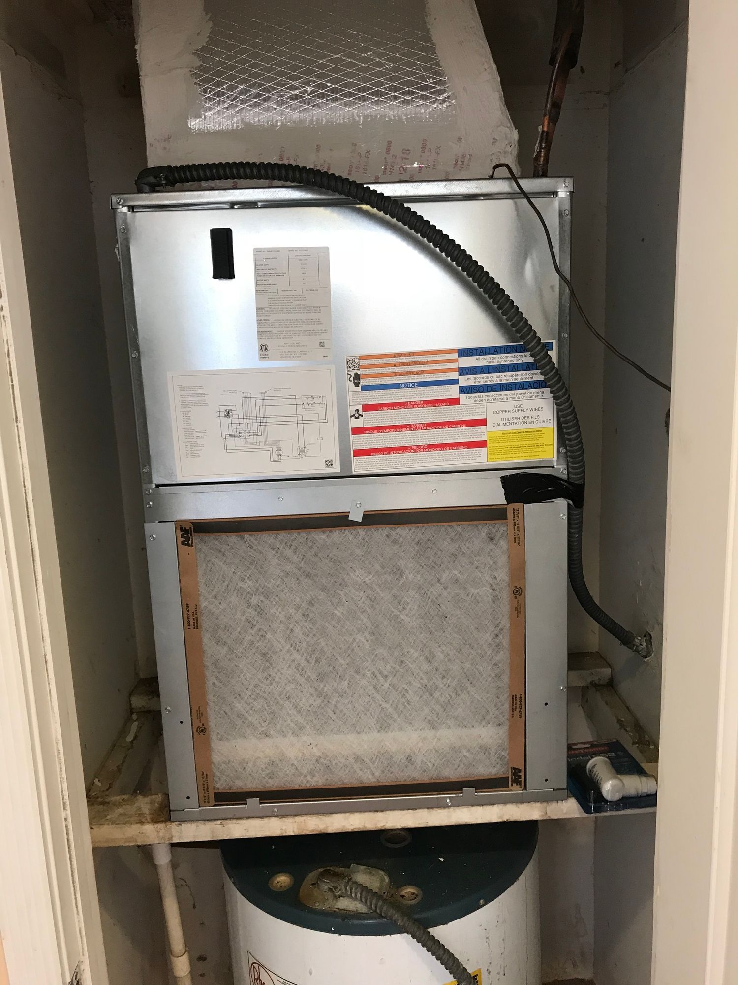 An air conditioner is sitting on top of a water heater in a closet.