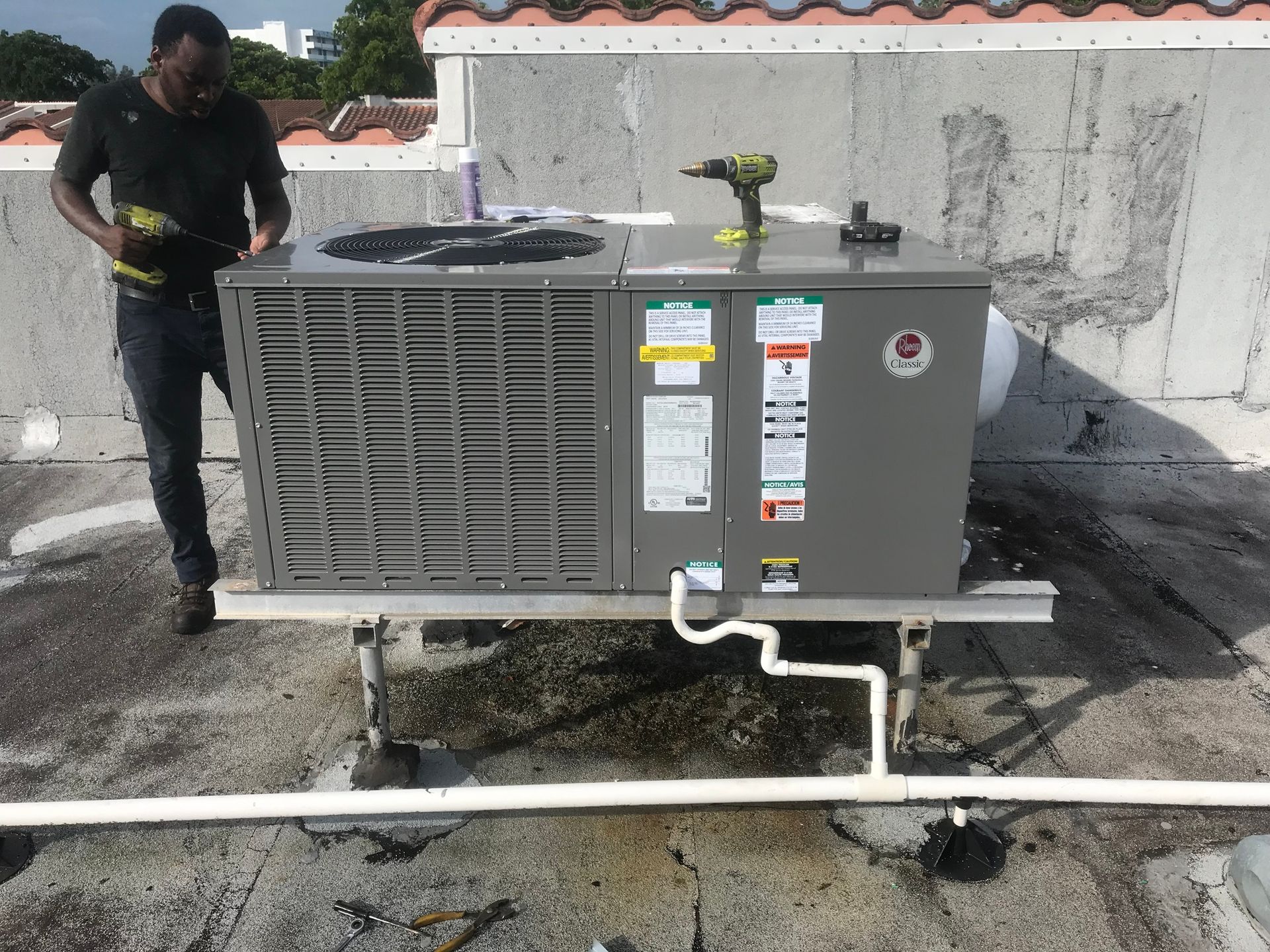 A man is working on an air conditioner on the roof of a building.