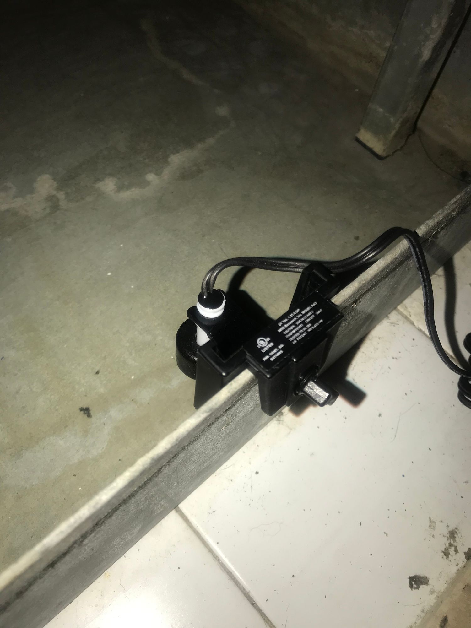 A black device is sitting on a tiled floor next to a wall.