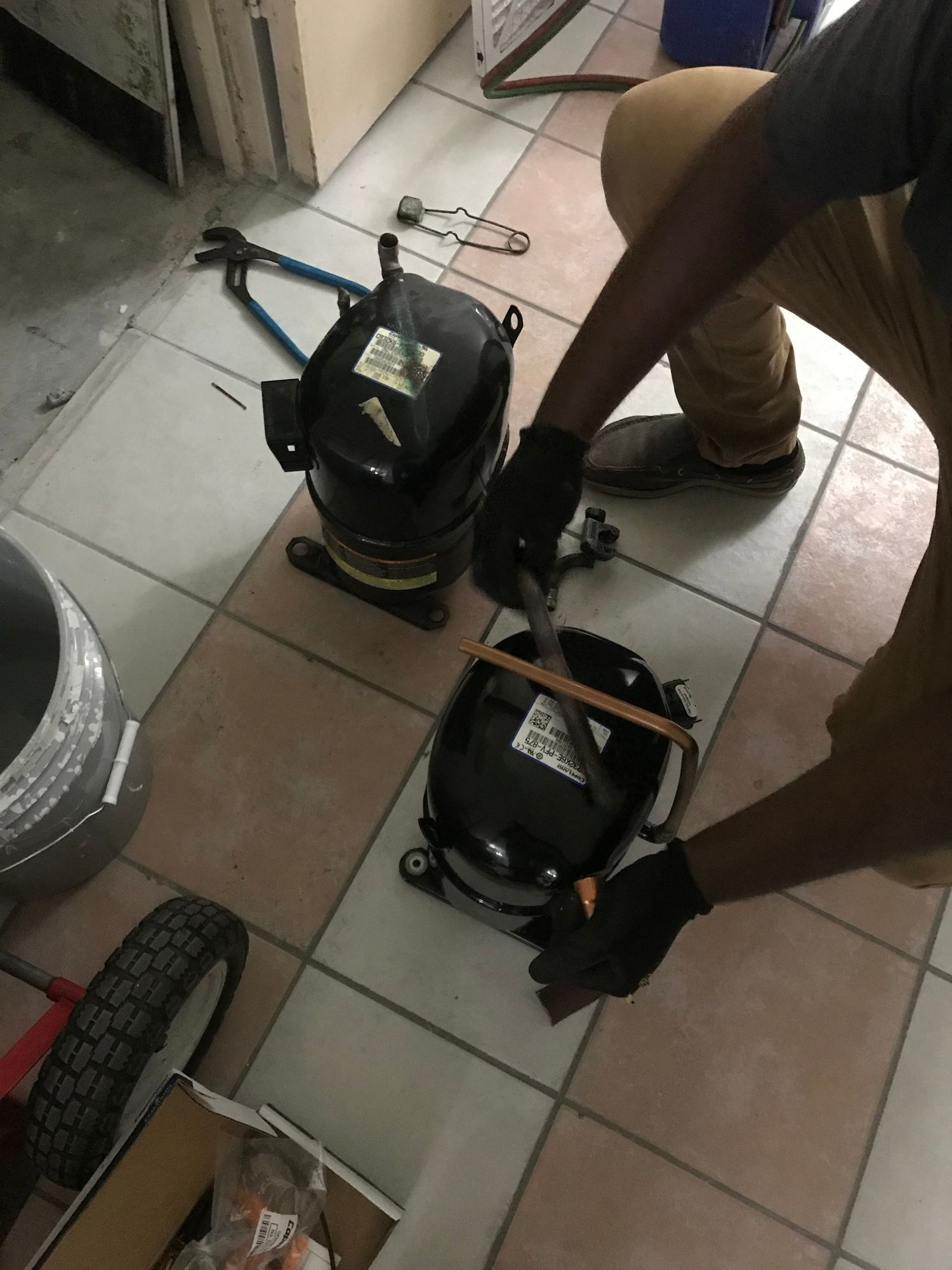 A man is measuring two compressors on a tiled floor.