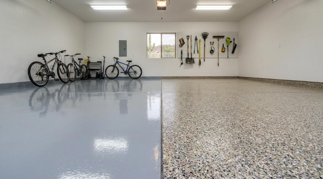 Garage with several bicycles, white walls, and a split epoxy floor of smooth gray and speckled tan.