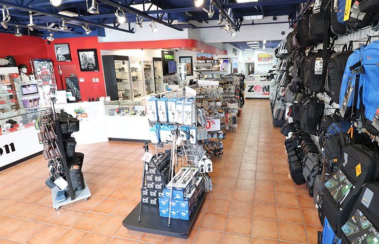 Intérieur d'un magasin de photographie avec un comptoir et une vitrine. On peut lire sur le comptoir « PHOTO » et « L'EXCELLENCE EN IMAGE ».