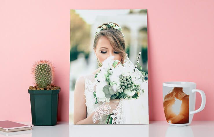 Une mariée tenant un bouquet blanc, sur une photo encadrée posée sur un bureau rose avec un cactus et une tasse à café.