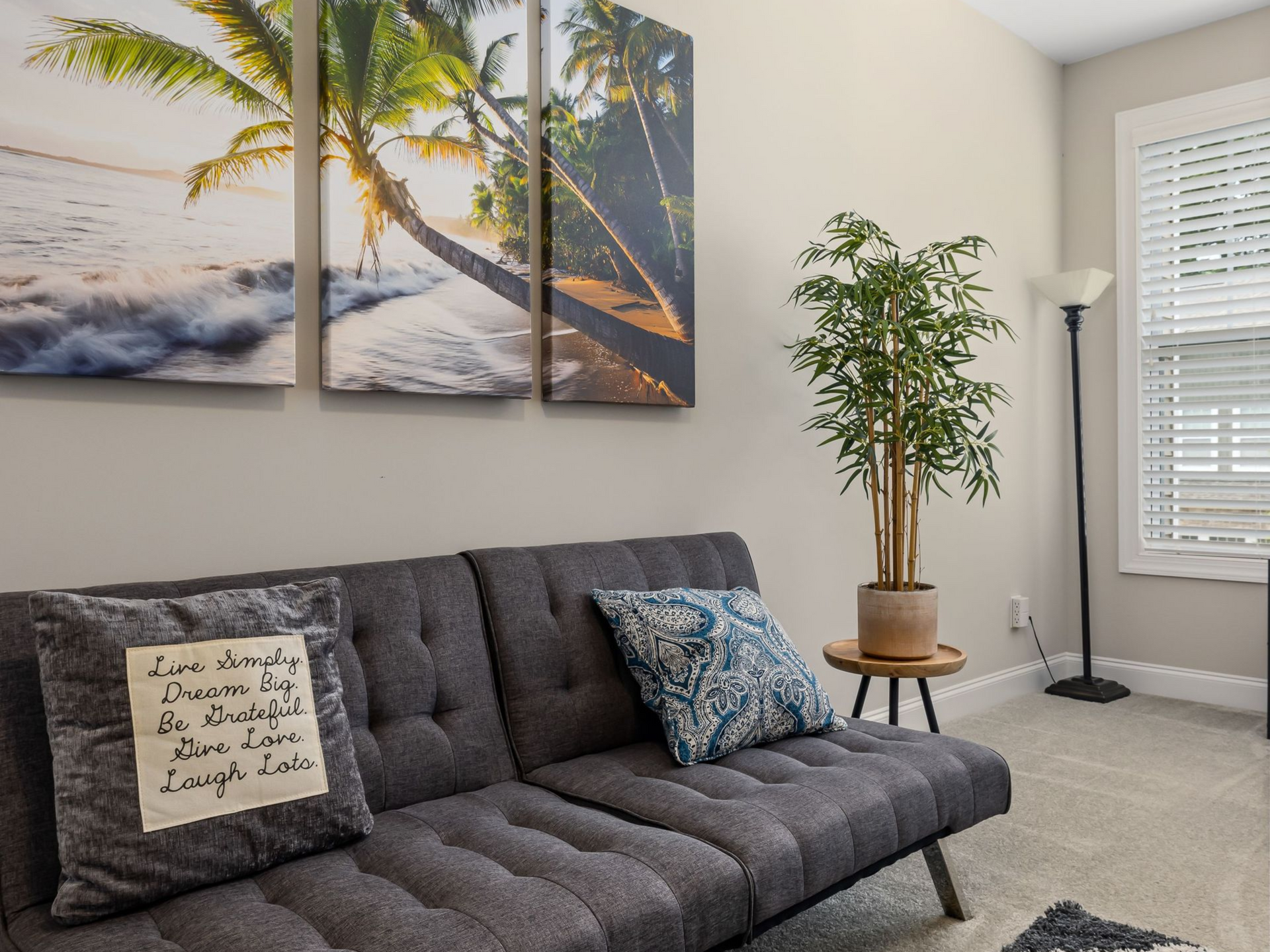 Salon moderne avec un canapé gris foncé, une décoration murale représentant un palmier et une plante en pot près de la fenêtre.