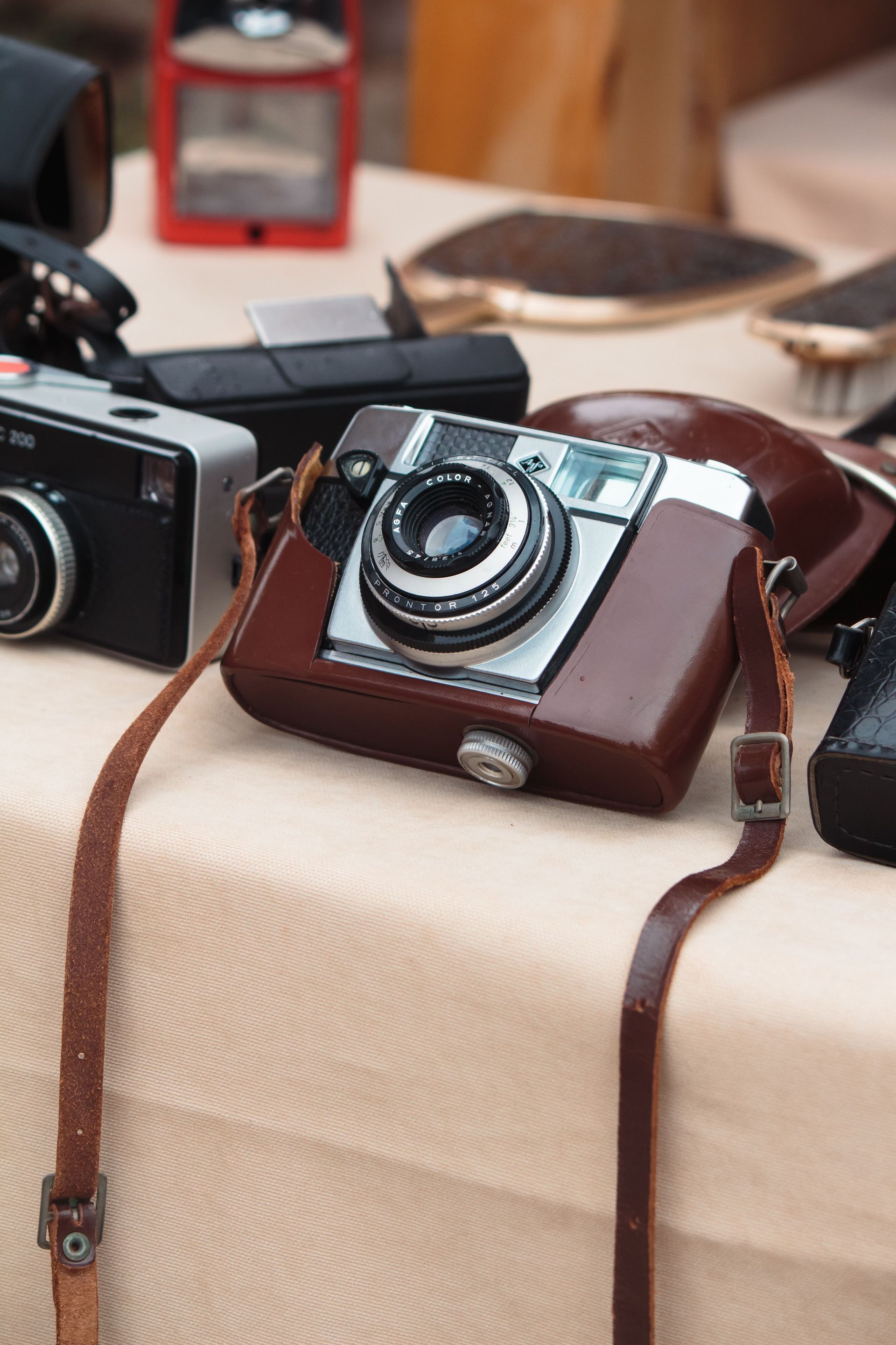 Un appareil photo vintage dans un étui en cuir marron posé sur une table, avec d'autres appareils photo et accessoires à proximité.
