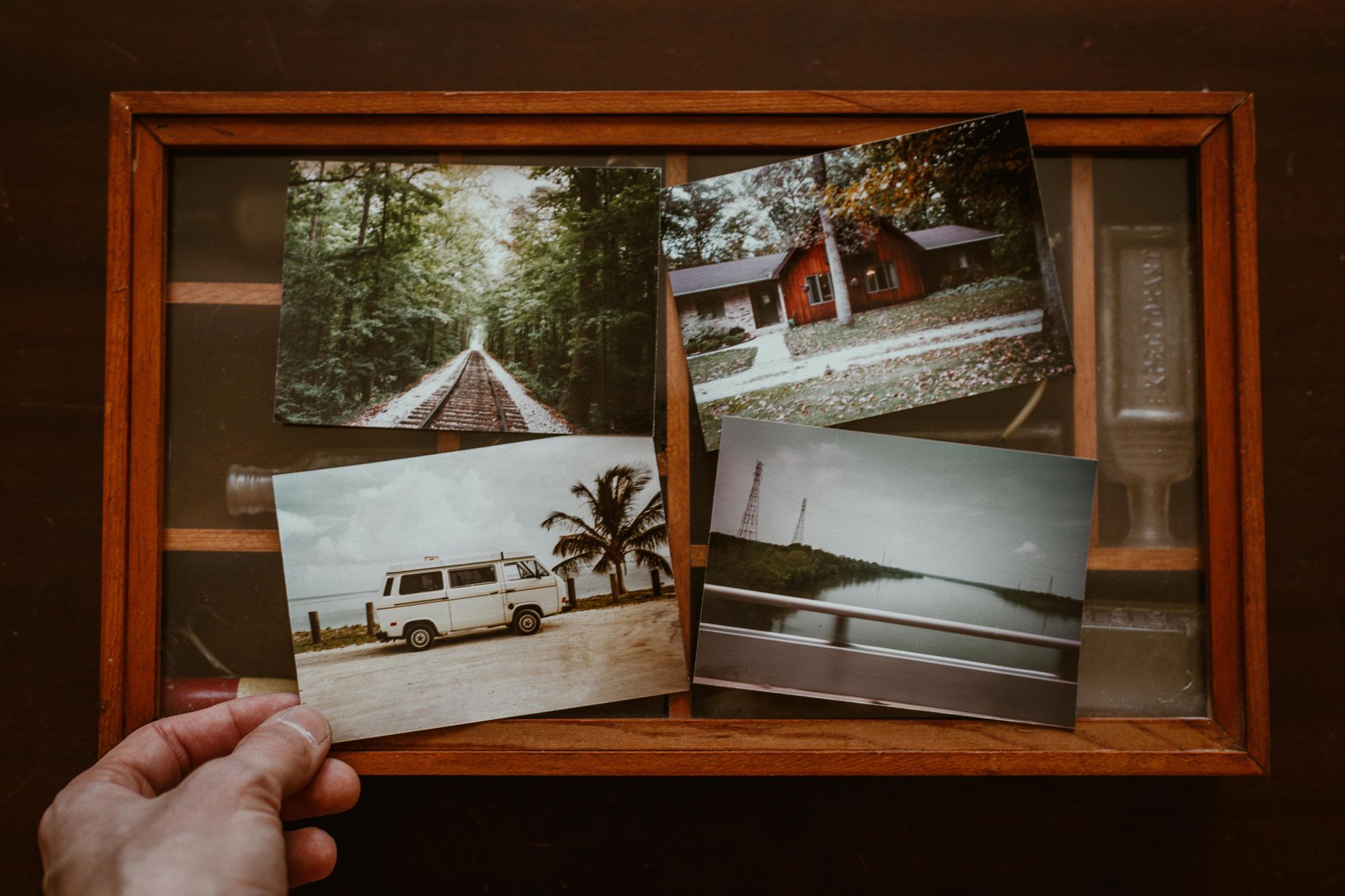 Main tenant une photo ; vitrine avec trois autres photos : chemin forestier, cabane, camionnette sur la plage et vue sur la rivière.